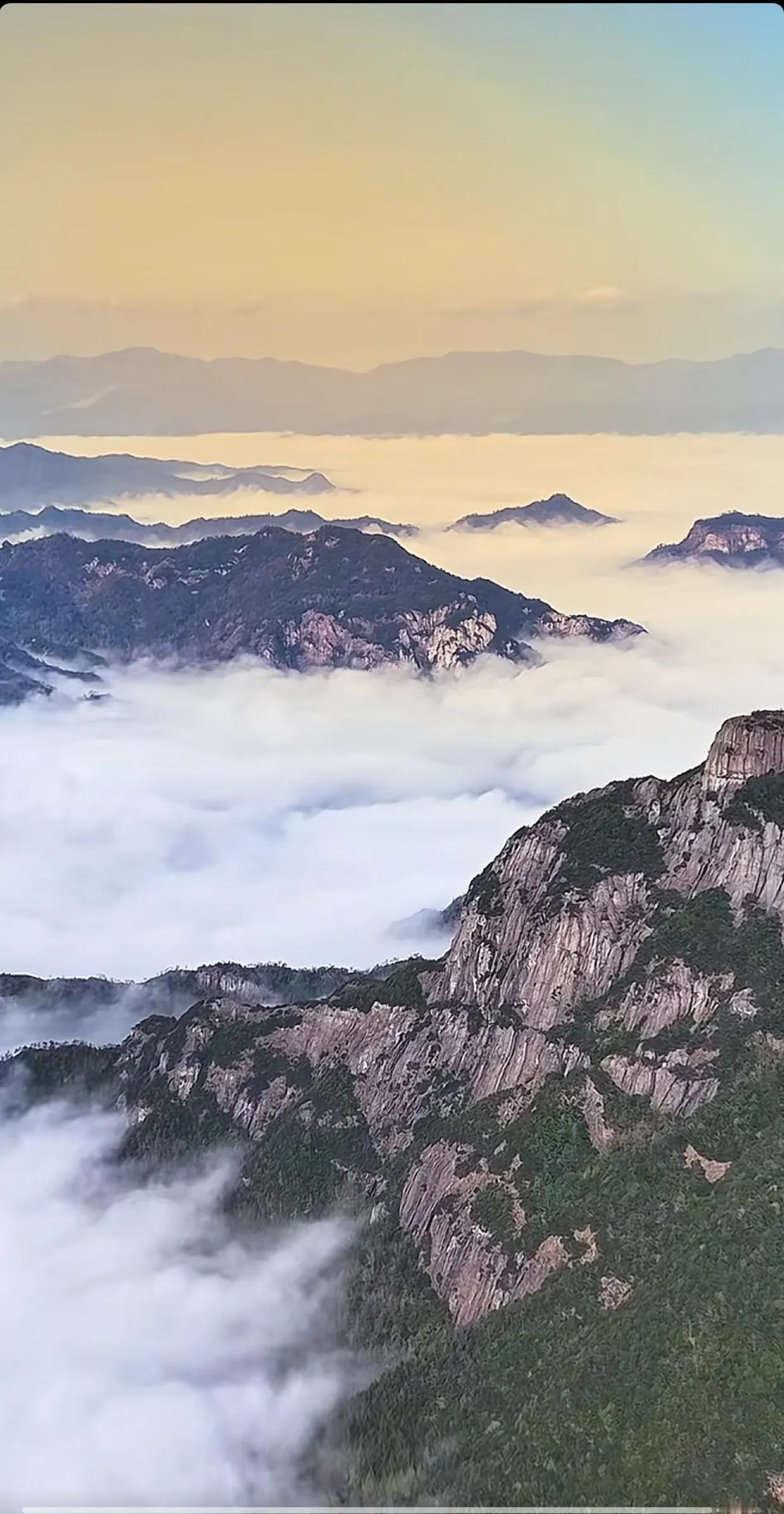 云海茫茫，阳光透过云层洒在群山之巅，如同仙境般梦幻。俯瞰天际，波浪起伏，美得令人