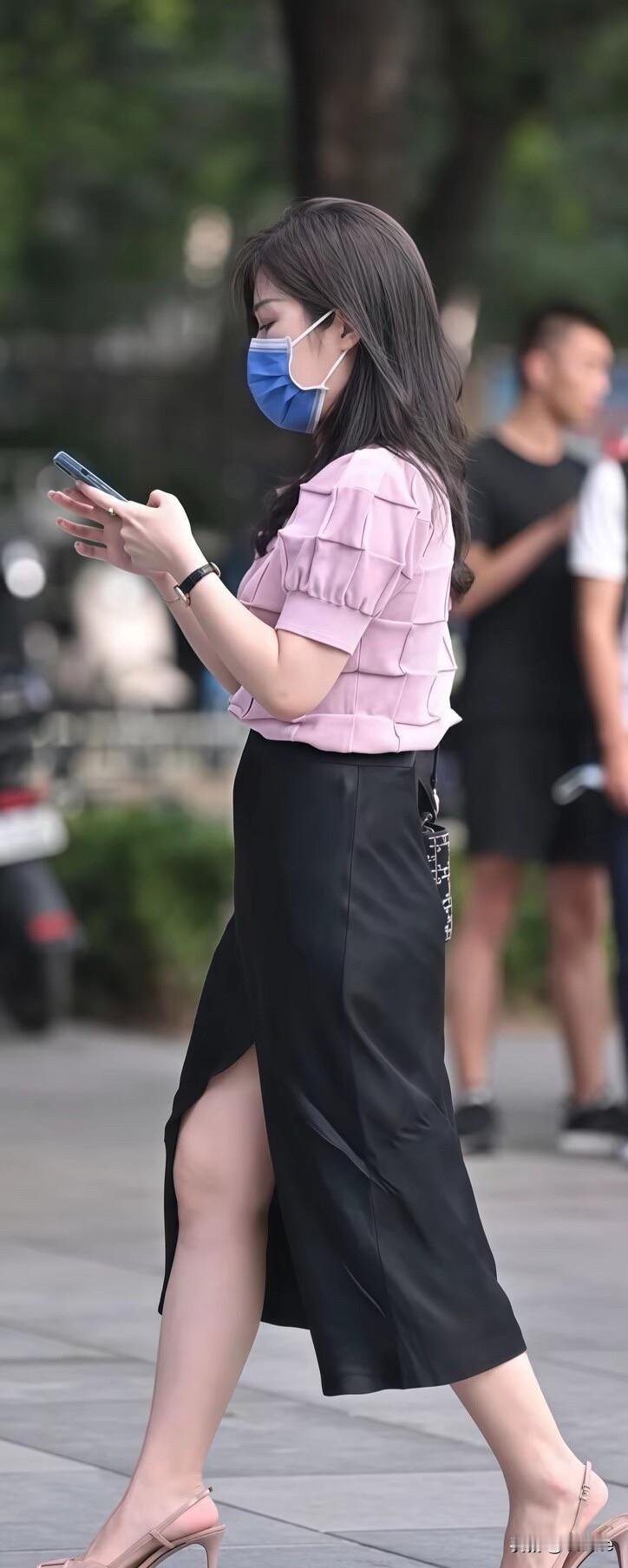 一个戴口罩的女士在走路看手机。