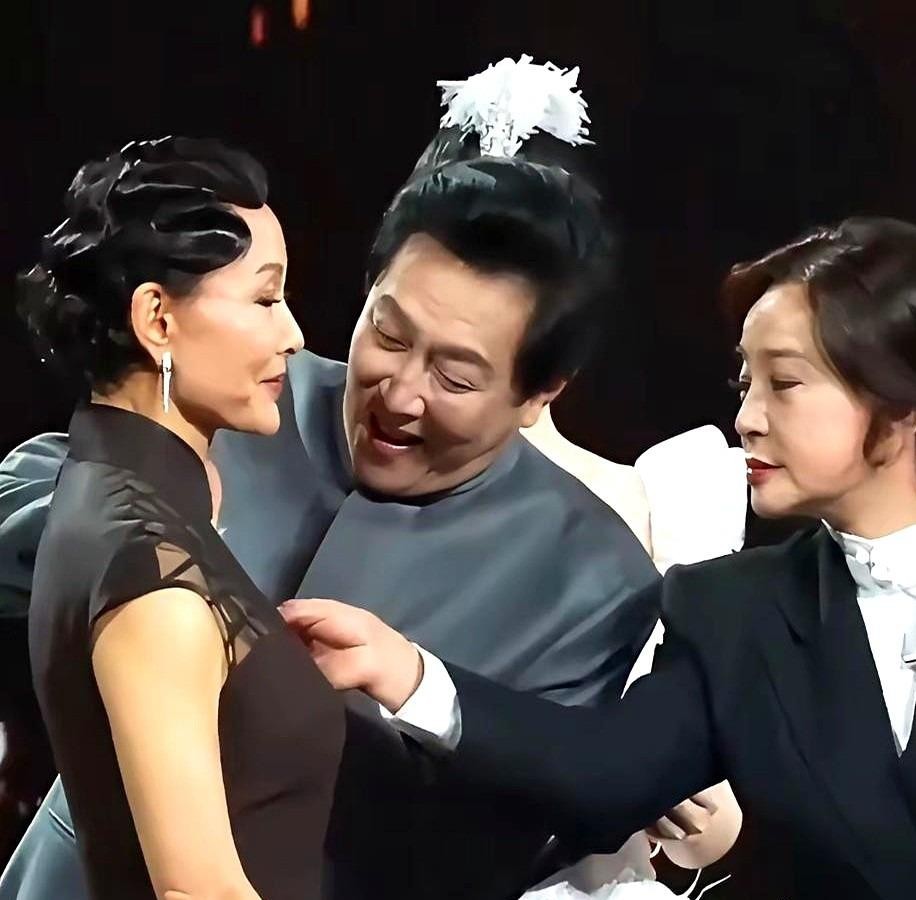 47年后，陈冲、唐国强、刘晓庆同台。胸前花饰毫无征兆脱落，唐国强俯身拾起，刘晓庆顺势侧身遮挡机位。无