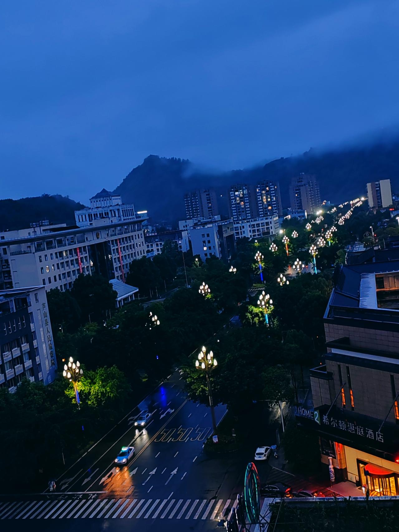暮蓝夜色漫过芦山城，雨后长街路灯成行，远山藏进薄雾，小城静谧温柔。这夜色，藏着安