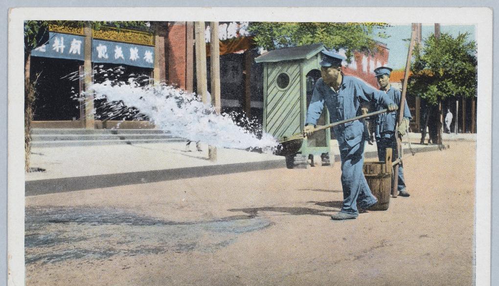 1920年，北京街头，两名警察正在清洁街道。他们抬来一桶水，一名警察用木勺将水泼