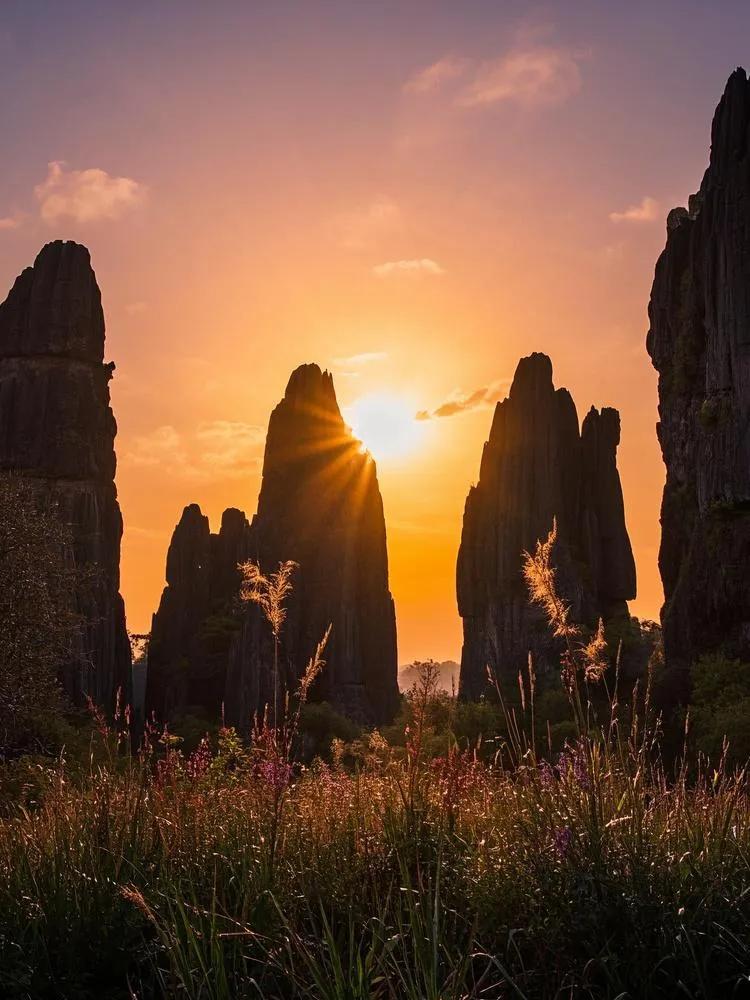 云南石林的傍晚，夕阳晕染天空，山上植物摇曳，为这片神奇之地增添梦幻氛围。云南自然