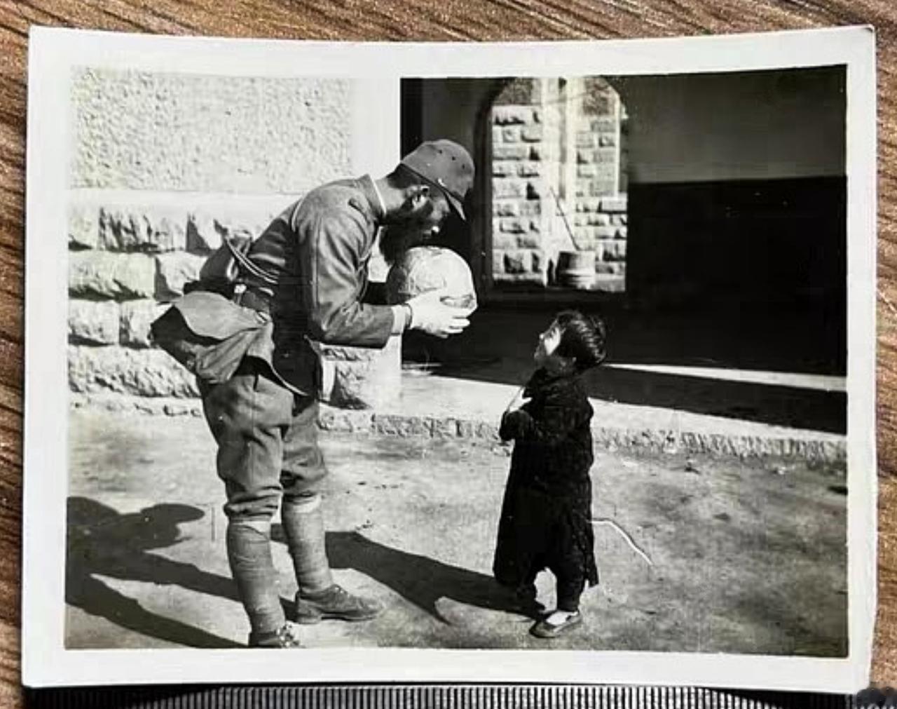 这是一张看似和平，实则残酷的照片。一名日军在村里遇到一位小女孩，他拿起一块大石头