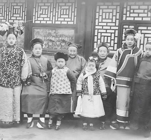 这张照片是清末北京旗人家庭的全家福，画面以一座雕花木棂的中式宅院为背景，窗格的几