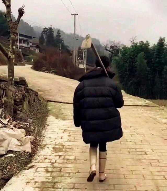 宁静扛着锄头回村了？！一身厚实的羽绒服，脚上踩着一双干净的小白靴，手里还拿着