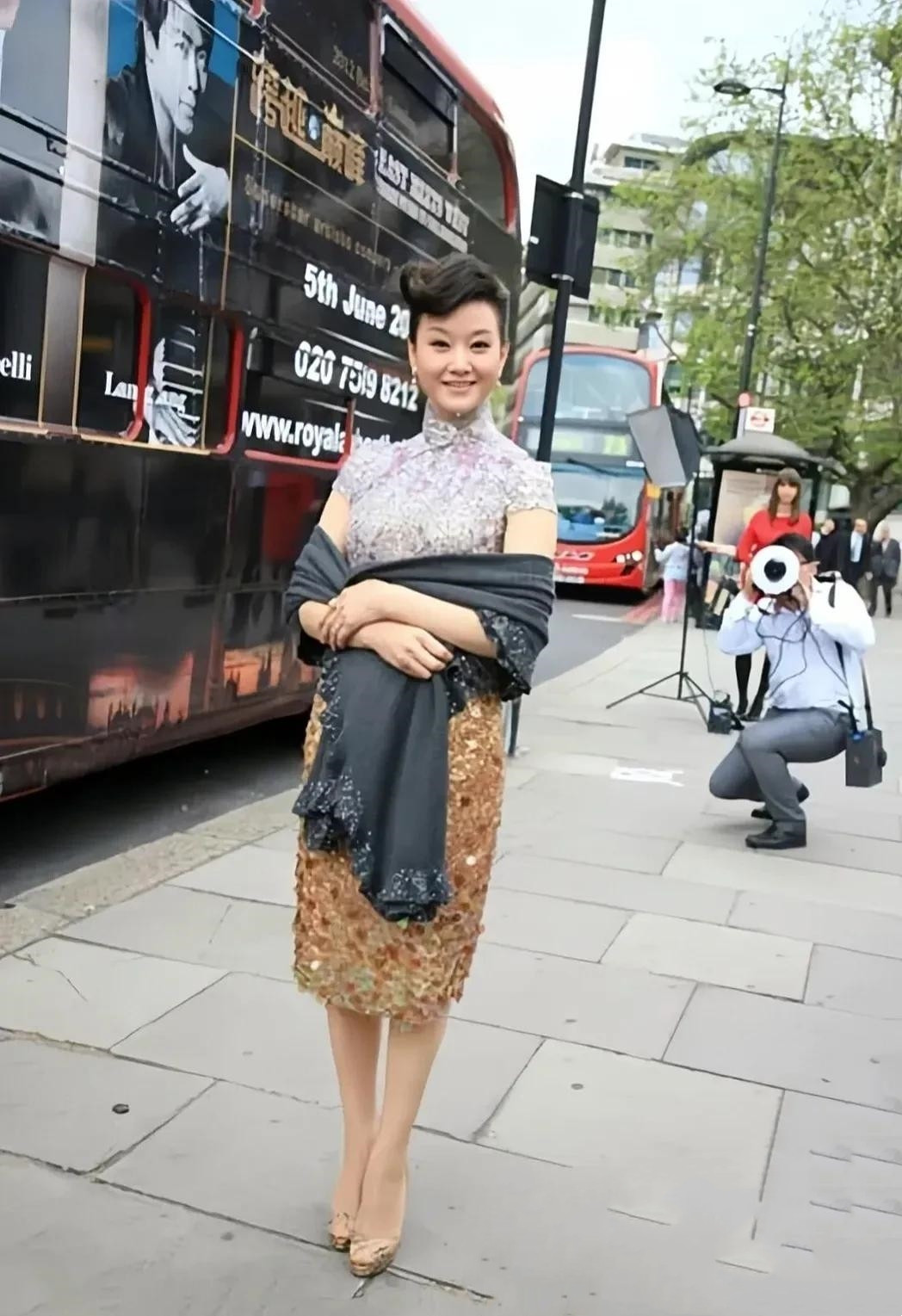 在英国街头偶遇50多岁歌唱家宋祖英。照片中，身着紫色棕色晕染亮片旗袍裙，搭配灰色
