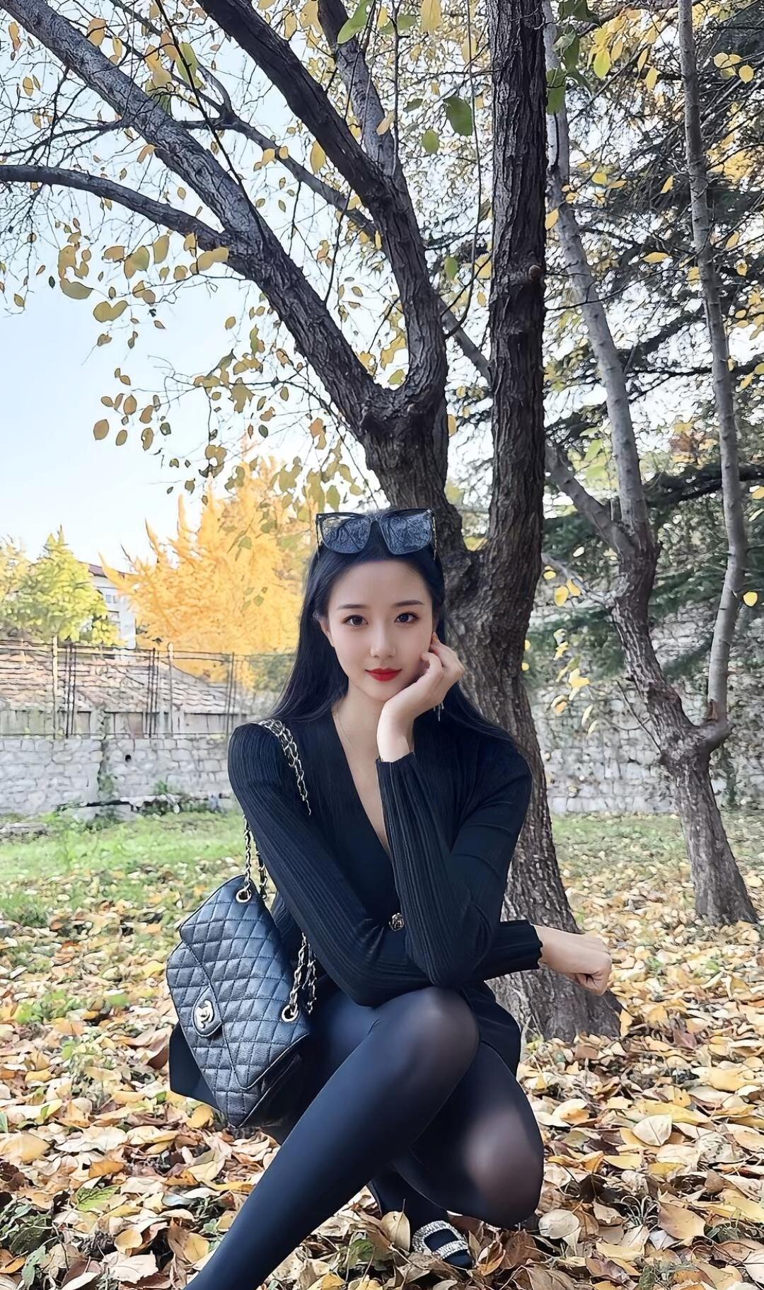 秋日暖阳下，黑衣美人倚树而坐，时尚感十足！