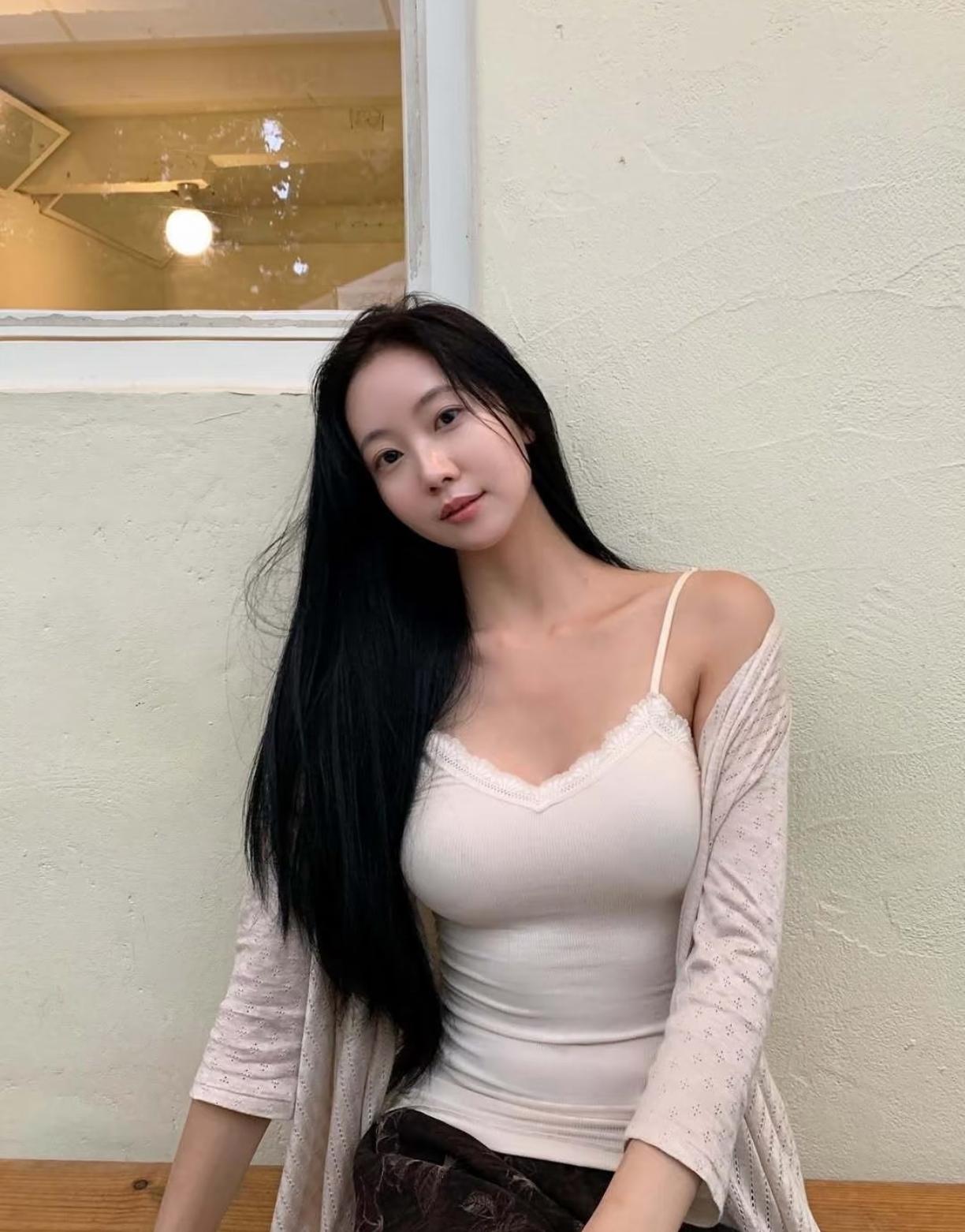 长发美女靠墙摆姿势，背景有窗户。