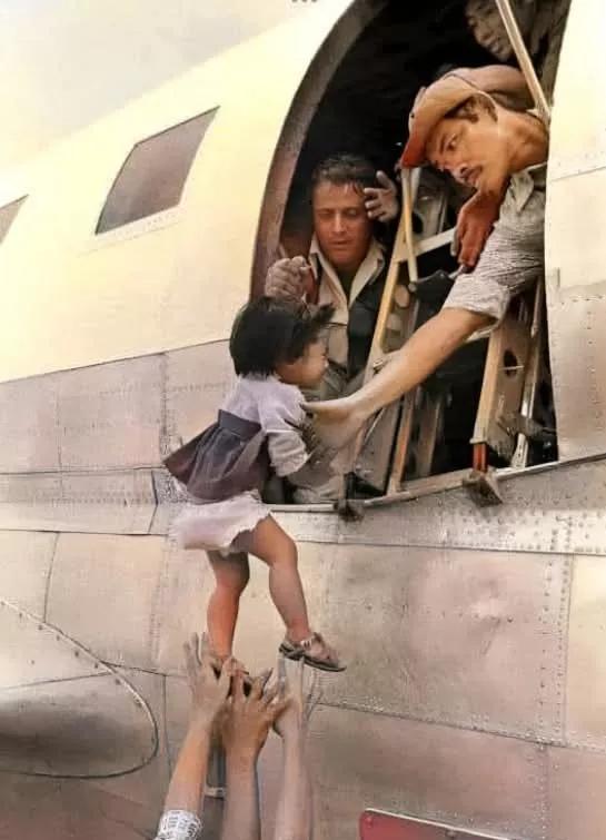 美军撤离西贡时，一个年轻的妈妈把一个婴儿抛向飞机的窗口，两个美国大兵伸手接往。