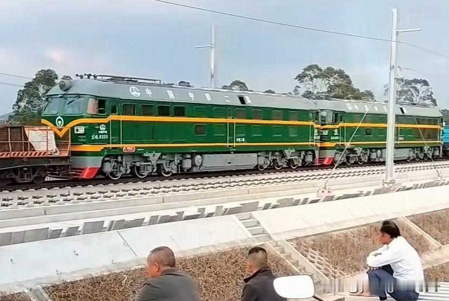 南珠高铁工地上，重联东风4B武警内燃机车正在牵引施工列车缓缓通过。旁边的居民们正