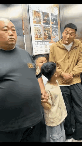 男孩在电梯间仔细观看黄衣男士做着的鬼脸，与男孩同行的父亲转过头来看他一眼，他一看
