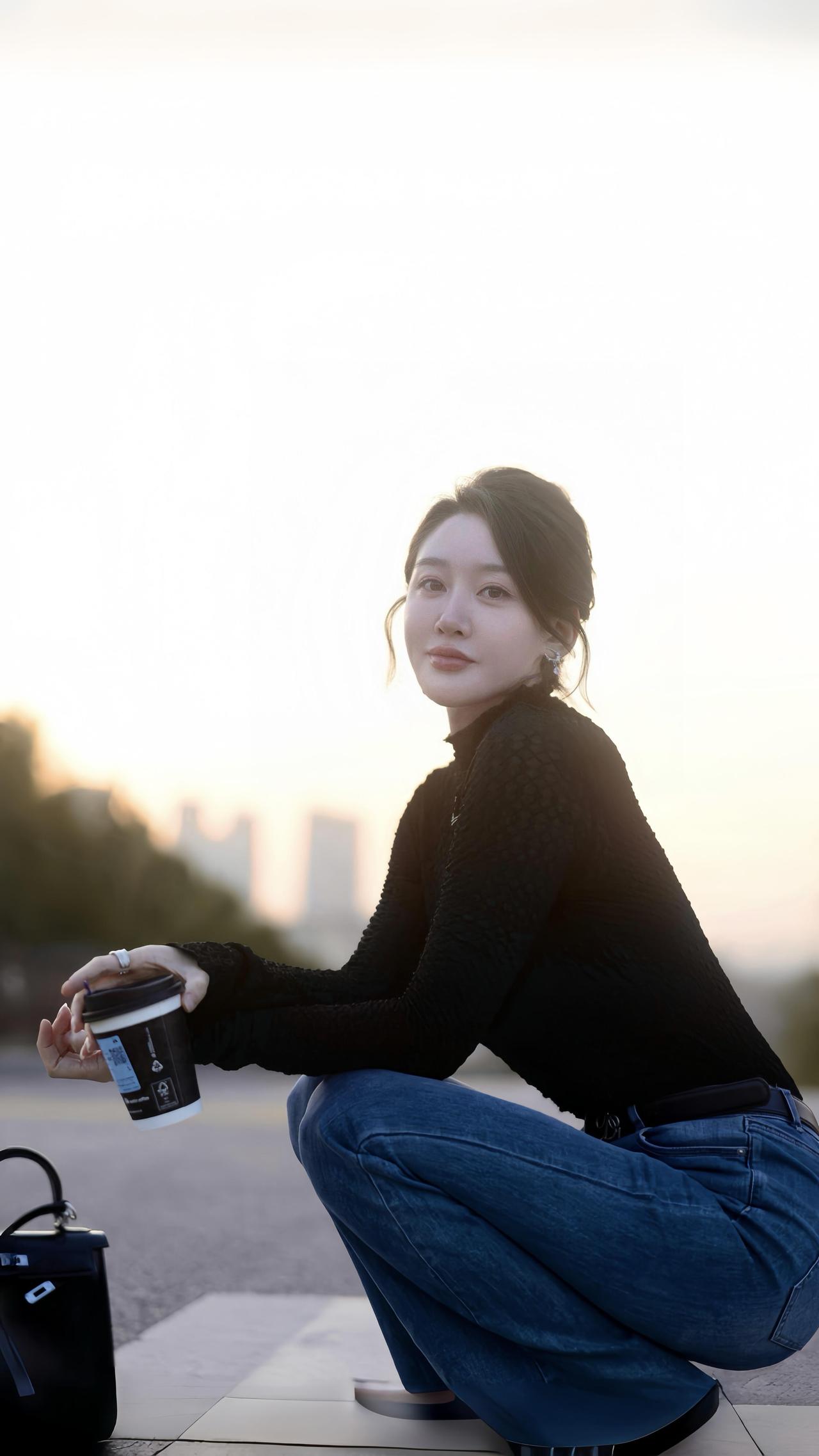 暮色晚风里黑针织的纹路裹住落日的余温牛仔蓝漫过路面，像揉皱的海她蹲在晚