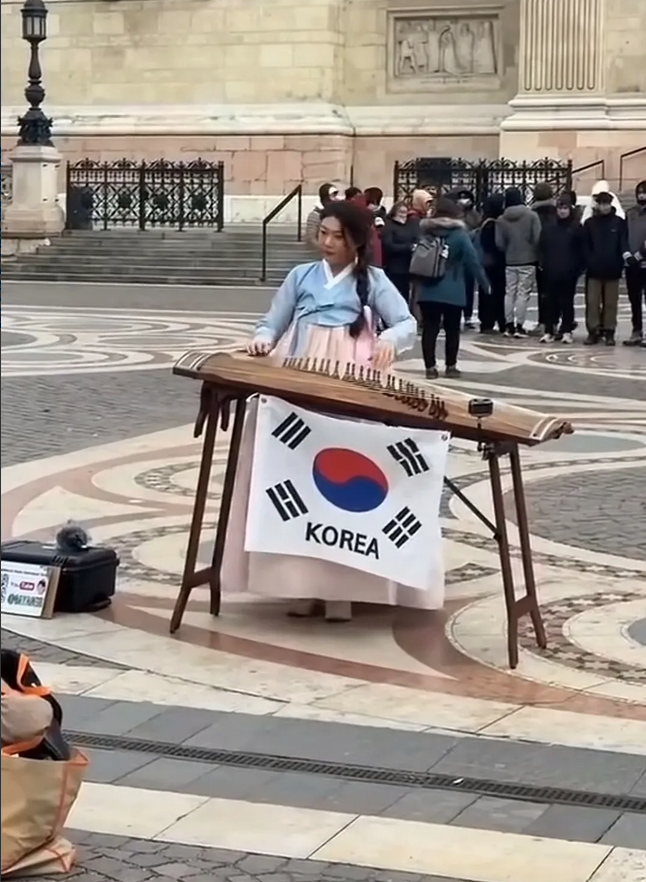 一位韩国主播身着传统服饰，在巴黎铁塔下弹古筝时悬挂韩国国旗引发关注。其演奏虽具
