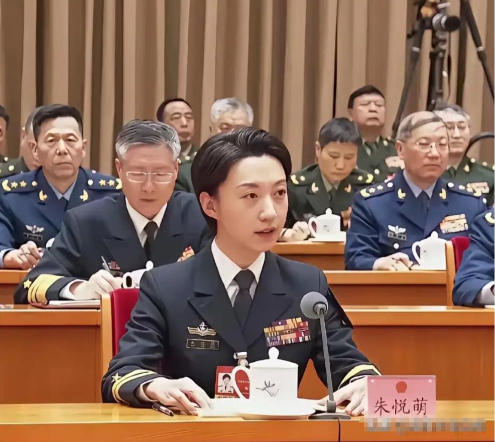 她在发言席上发言，背后将星云集。她是辽宁舰第一批女舰员，曾是全舰唯一女基层主官。
