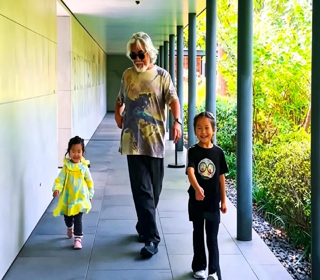 张纪中在自家庭院长廊，陪着两个女儿练习模特步。一开始小姑娘走路都很正常，跟着他学