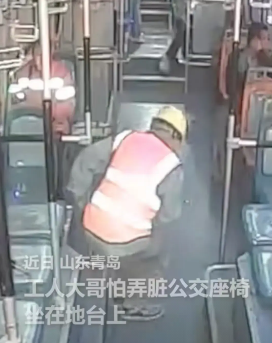 令人泪目！在山东青岛的一辆公交车上，一位工人大哥因担心弄脏座椅，选择坐在地台上，