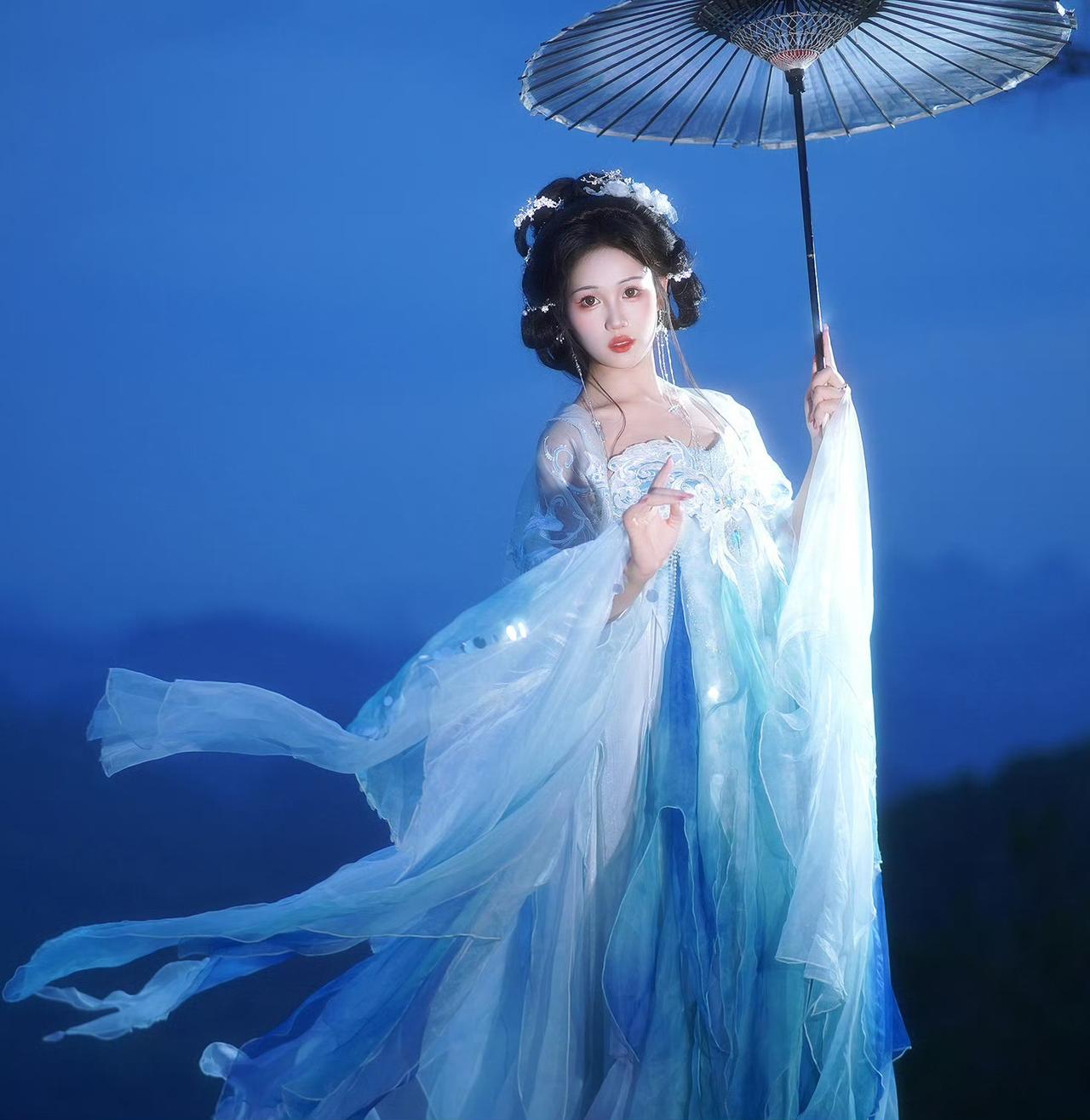 暮色染蓝山巅，她立于崖边，一身水色罗裙随风舒展，如月光下漾开的清涟。油纸伞轻