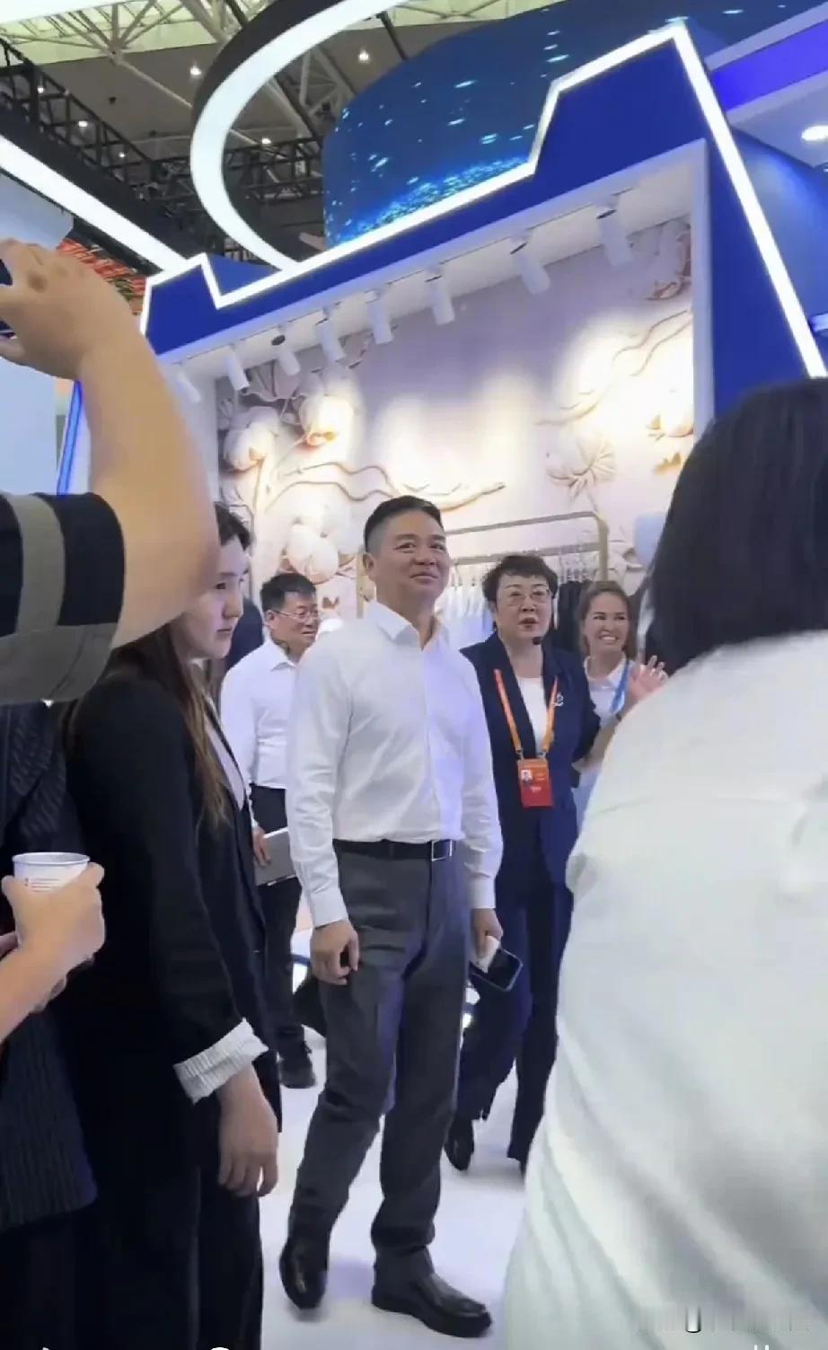 刘强东现身展会啦！人群中他身着简约白衬衫，搭配利落西裤，身形笔挺，气场沉稳。近距