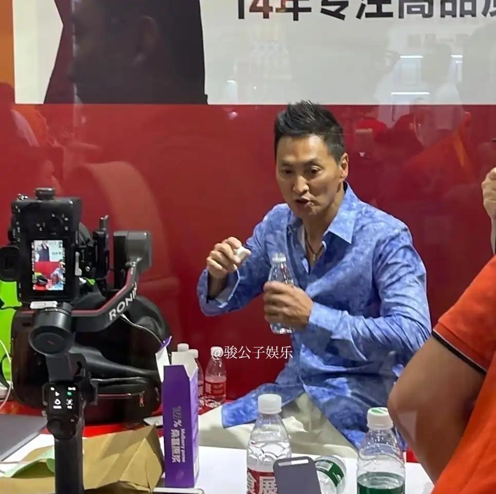65岁的何家劲近日在上海食品展上惊艳亮相，身着蓝色花衬衫搭配油头造型，胸肌饱满，