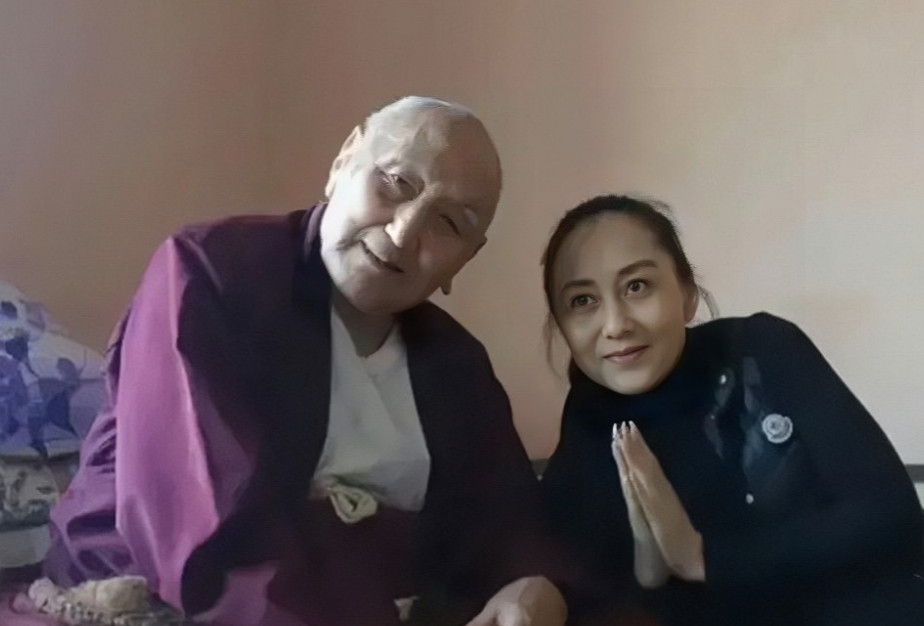 利智素颜照，镜头下的她身穿黑色外套，头发全部束起，双手合十，正在尼泊尔和李连杰一