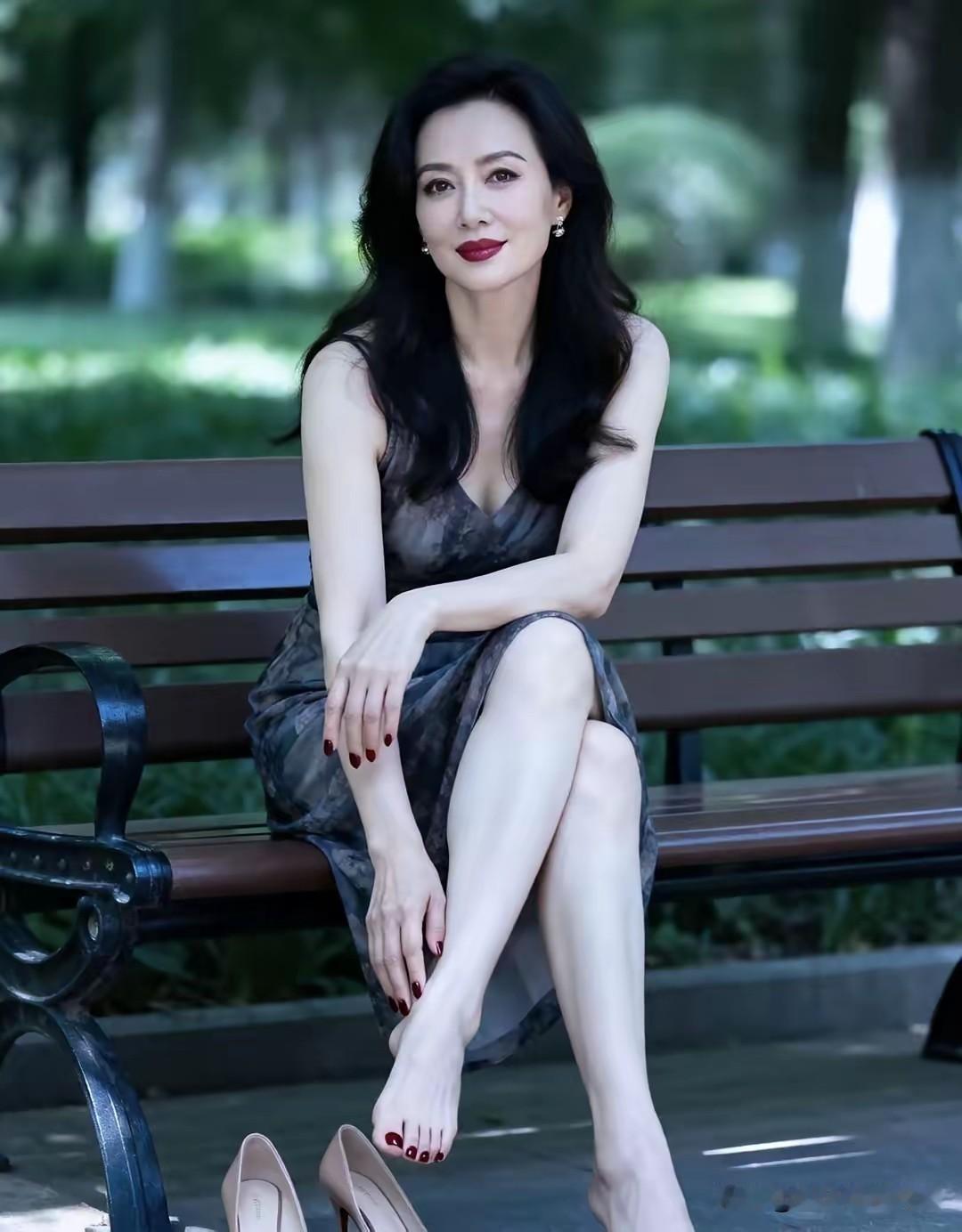 林荫光斑落在长椅上，把这份成熟女性的松弛感衬得恰到好处。一袭灰调晕染的无袖纱裙轻