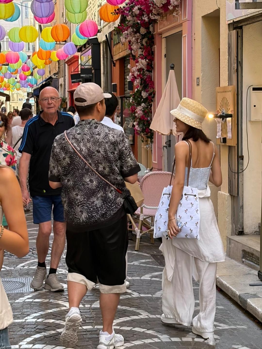 赵今麦和一男性友人现身法国南部旅游，她头戴法式麦秆帽，白色吊带长裙，背着单间背包