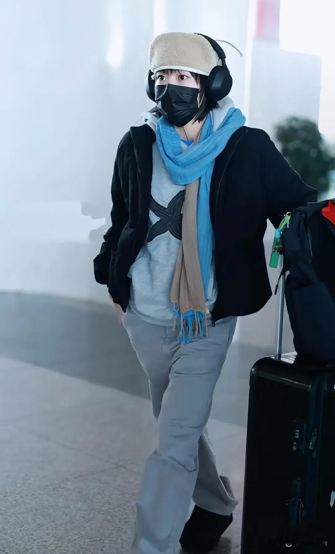 窦靖童现身机场，留着短发，穿着一身灰色的休闲装，头上戴着帽子和耳机，脚踩雪地靴，
