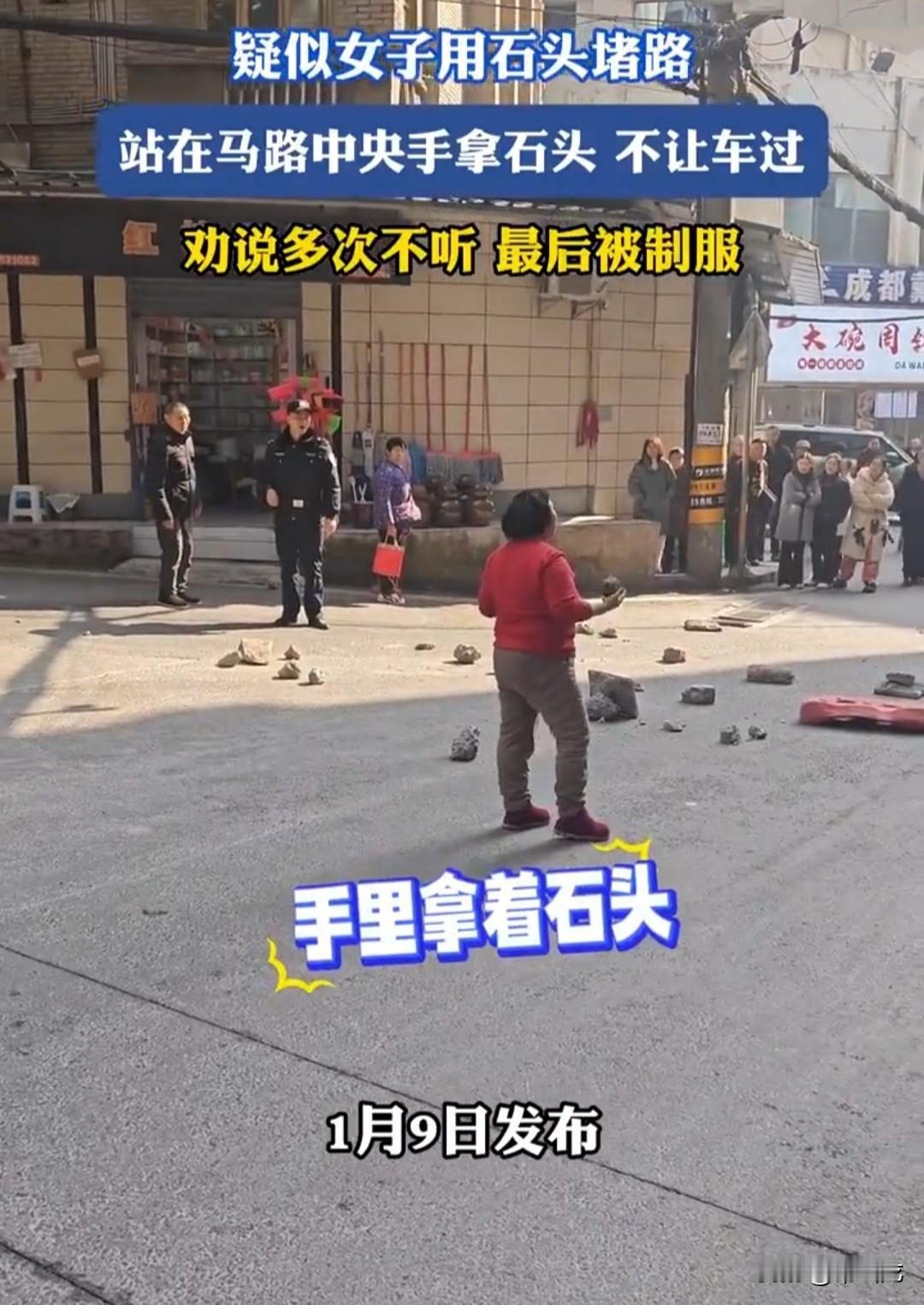 女子把石头摆放在马路中央堵着路，不让车辆通行，手里还拿着两个比鹅蛋还大的鹅卵石，