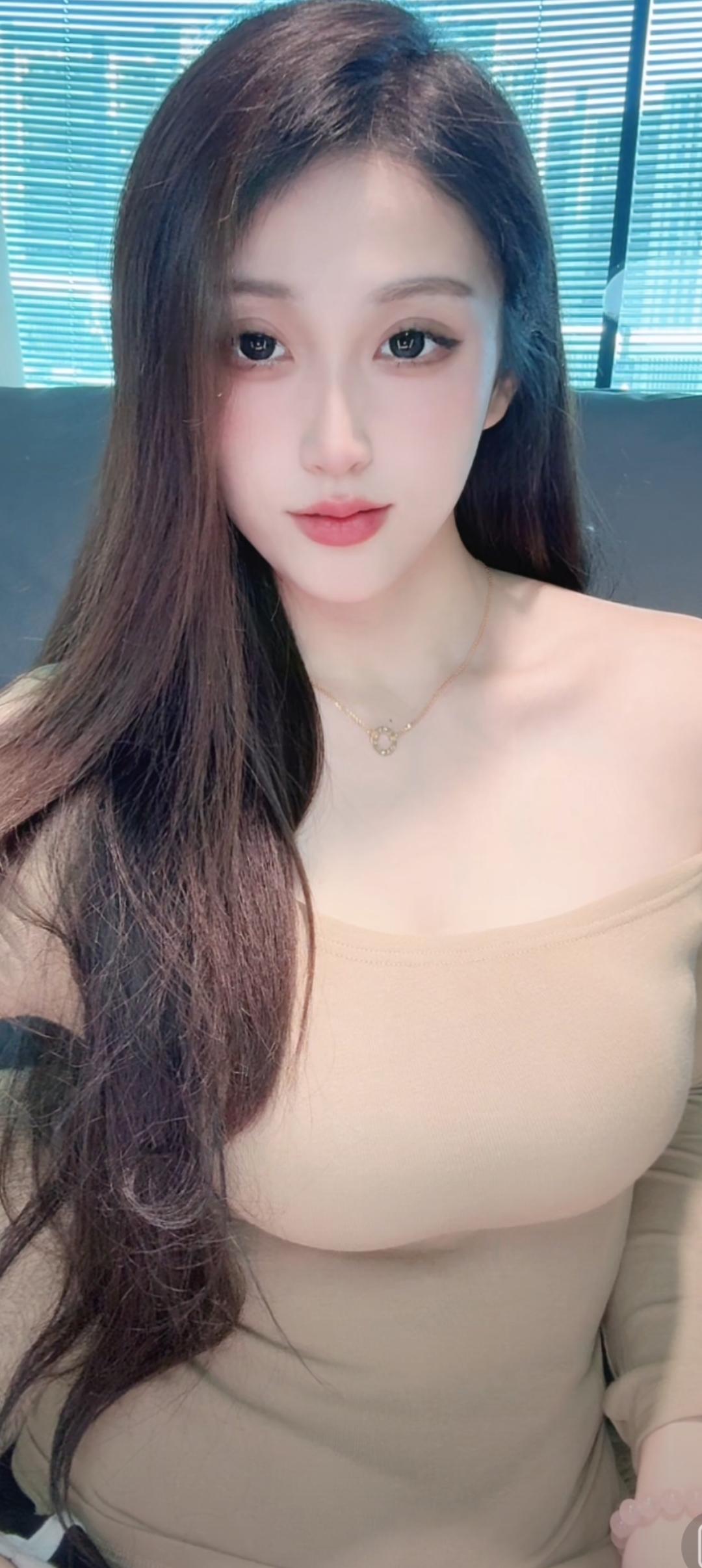 长发美女穿着吊带衫，坐在窗边。