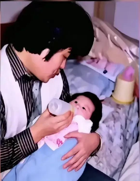 刘欢一只手抱着襁褓中的女儿，一只手拿着奶瓶喂女儿喝奶，那双弹钢琴的手，纤长秀气又