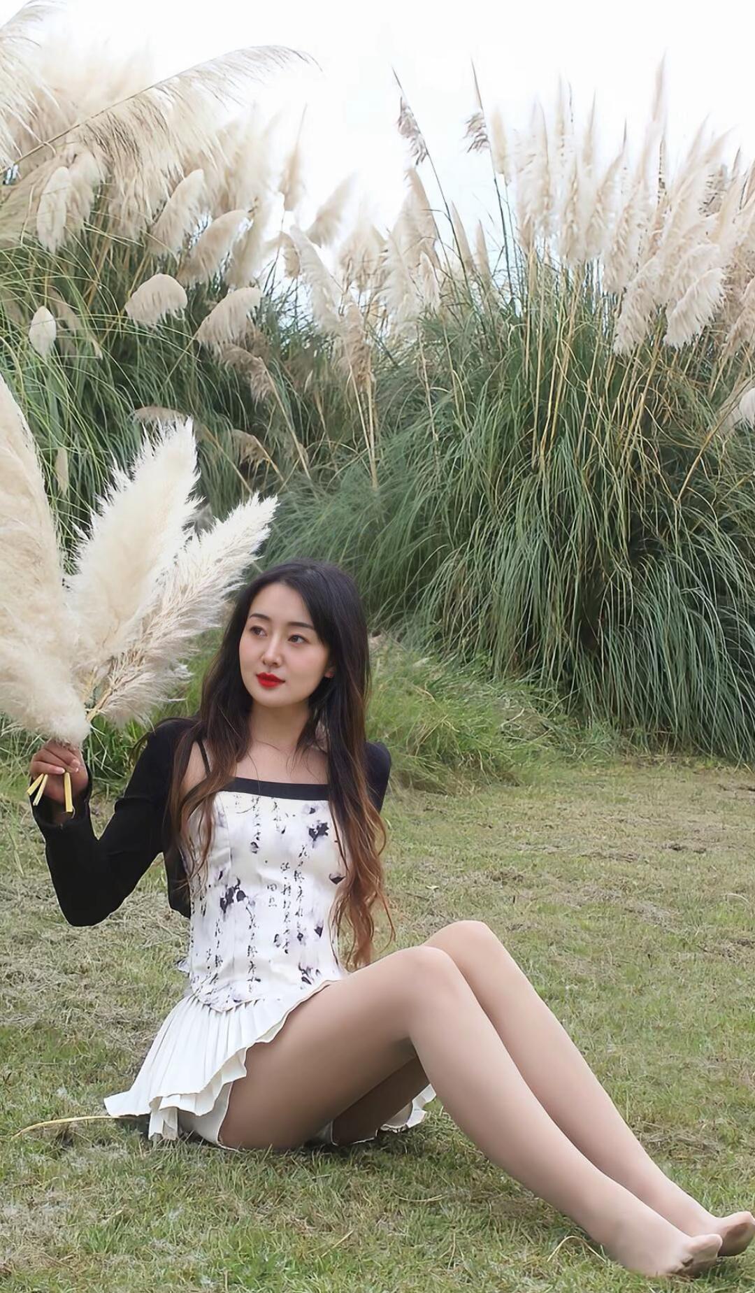 在草地上，她手持芦苇，温柔地微笑。