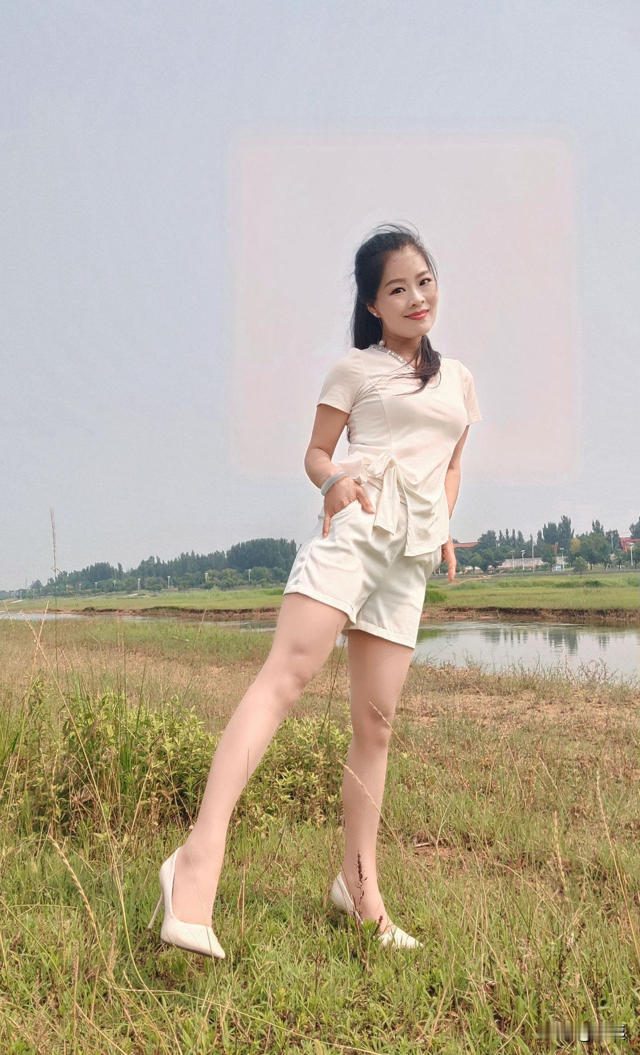 她穿着白色衣服，在草地上摆姿势。