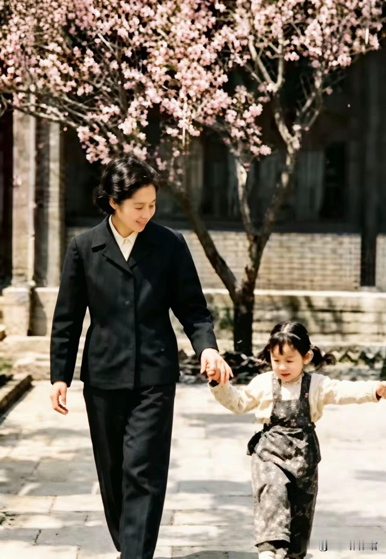 春日庭院繁花盛放，王光美牵着年幼女儿漫步石板小路，女子着装端庄素雅，孩童活泼轻快