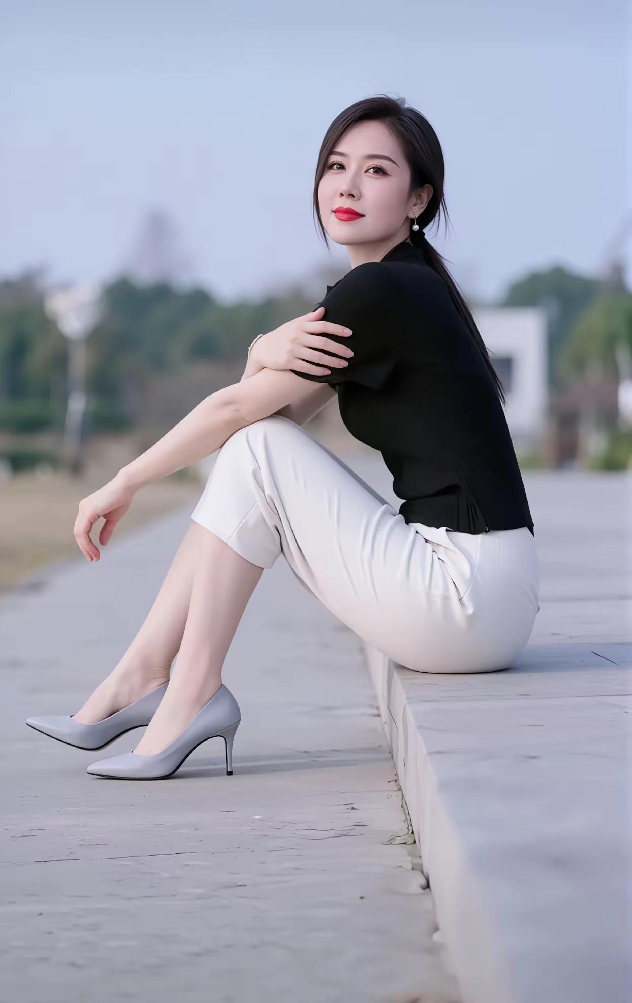 优雅坐于石阶上，黑衣白裤，高跟鞋，红唇微笑，享受宁静时光。