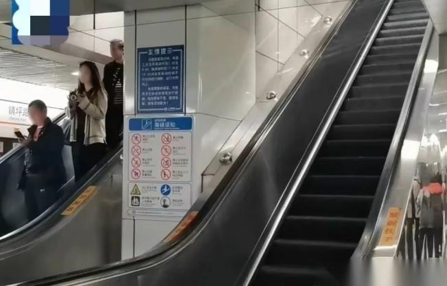 上海，男子在乘坐地铁站的上行自动扶梯时，前方的一位阿姨因站立不稳，突然向后倒去，