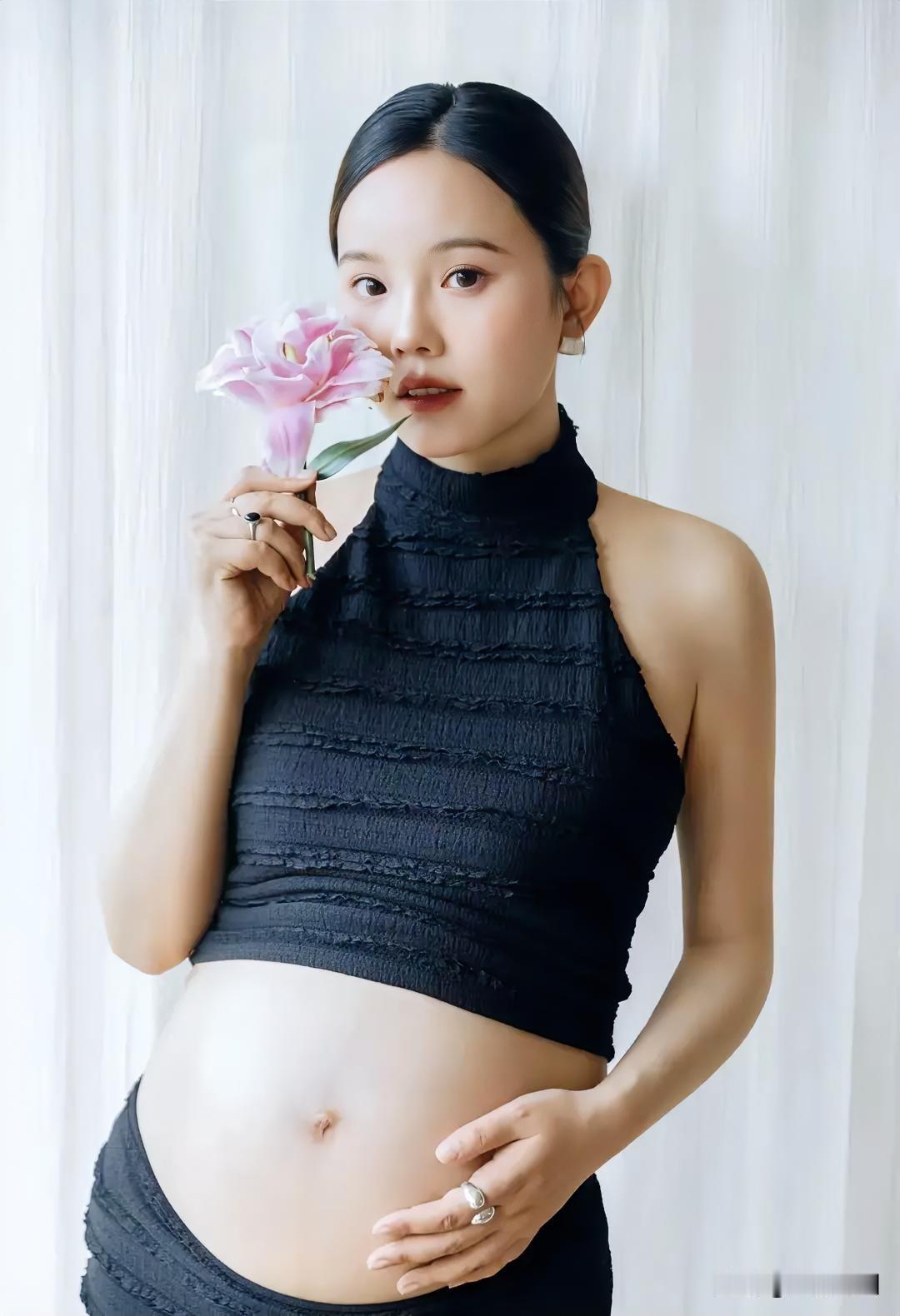 这位美女孕妇拿着粉色花摆姿势。
