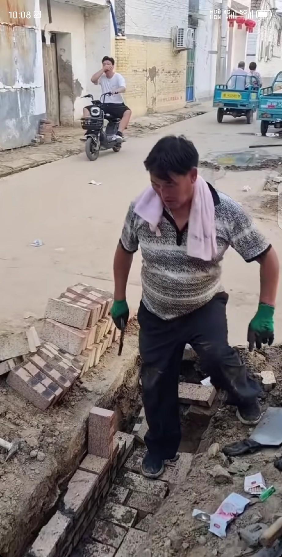 大衣哥朱之文又做善事了，在村里砌水沟呢！就他一个人，蹲那儿一块砖一块砖地垒，手上