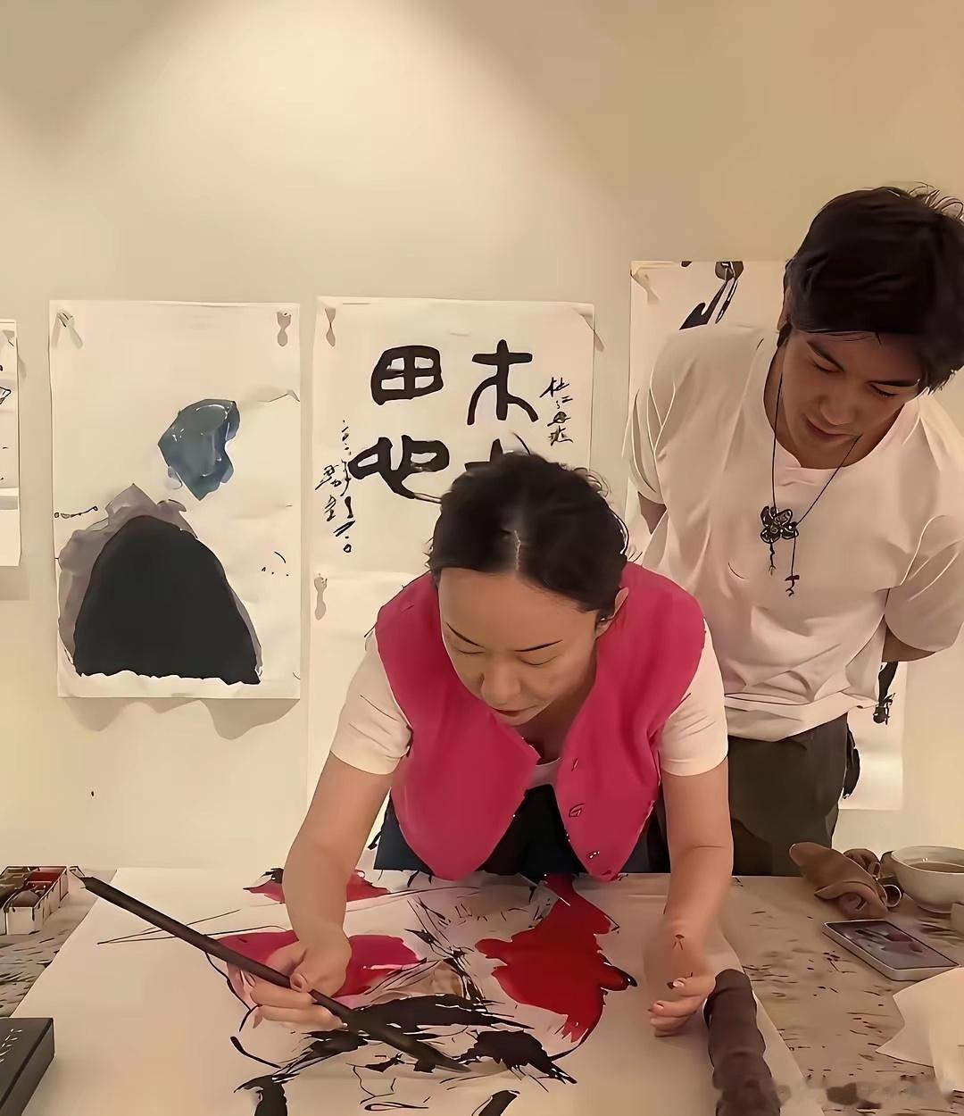 霍思燕在家中书房作画时的一幕，俯身手持大毛笔在宣纸上创作国画，丈夫杜江背手站在身