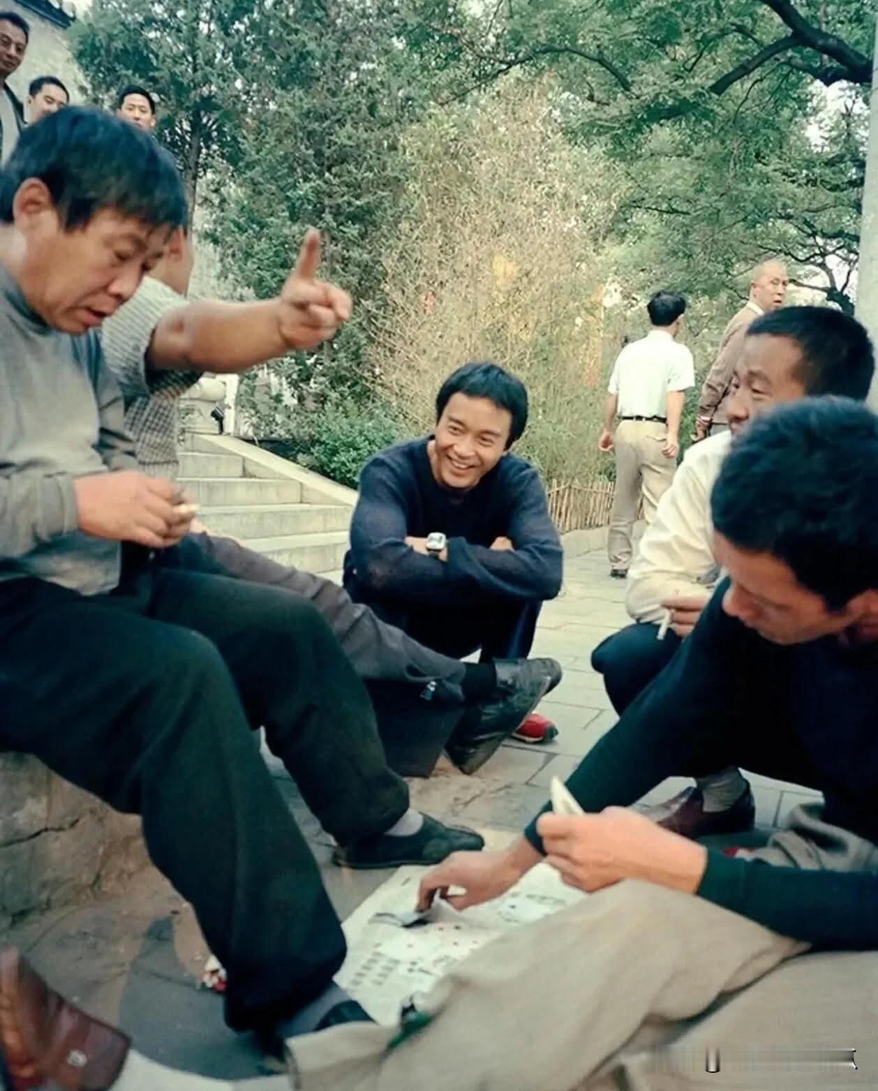 这张照片拍摄于2000年的北京公园门口张国荣蹲在地上看大爷们打牌满脸洋溢着笑