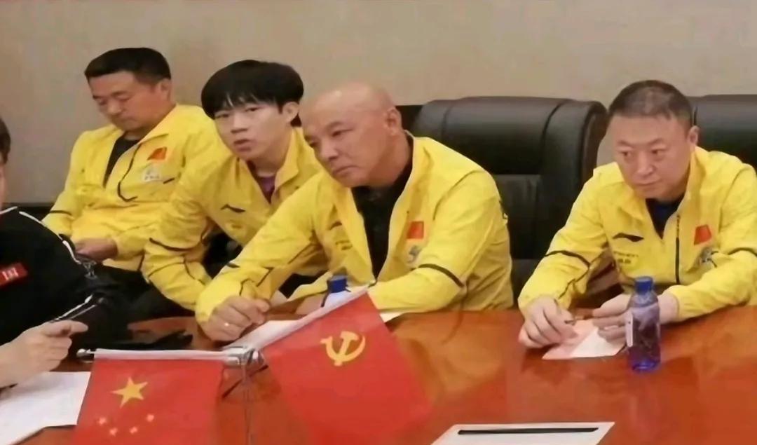 这应该是昨天在公园参加活动之后开会的场景。运动员和教练员都穿着厚厚的长袖队服，