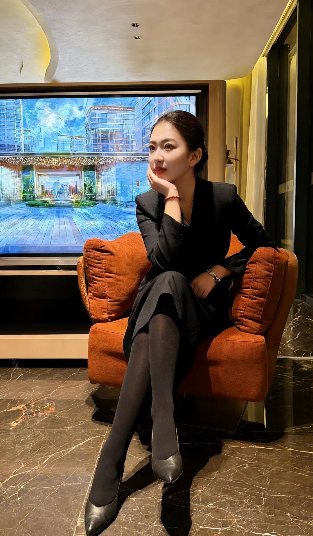 黑西装与黑丝勾勒出利落的轮廓，倚坐于暖调的沙发，让职场的干练与休憩的慵懒相融，在