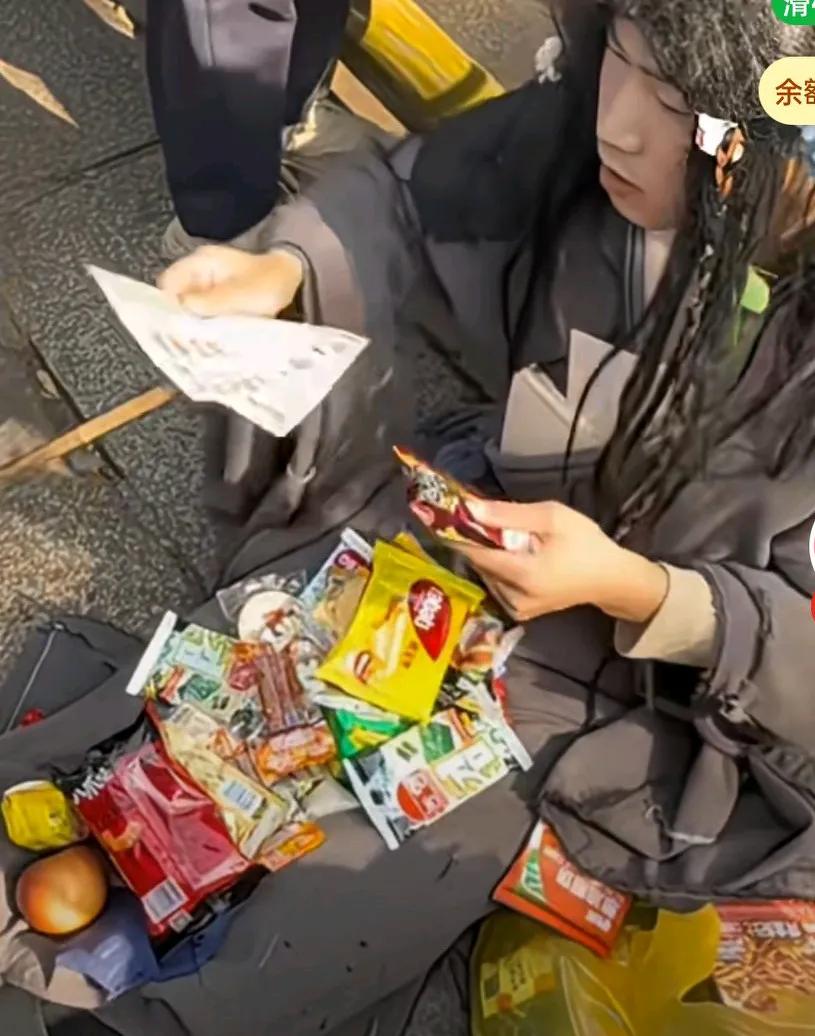 景区扮演乞丐的NPC，游客投喂到零食没地方放，只见他边吃边收零食，旁边的小孩子