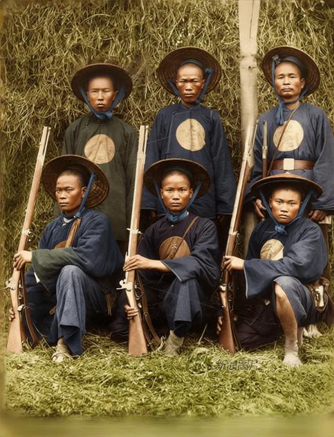 这帧老照片里，是法国殖民军队招募的当地黄旗军人员，聚在荒疏的草垛旁，宽大的斗笠遮