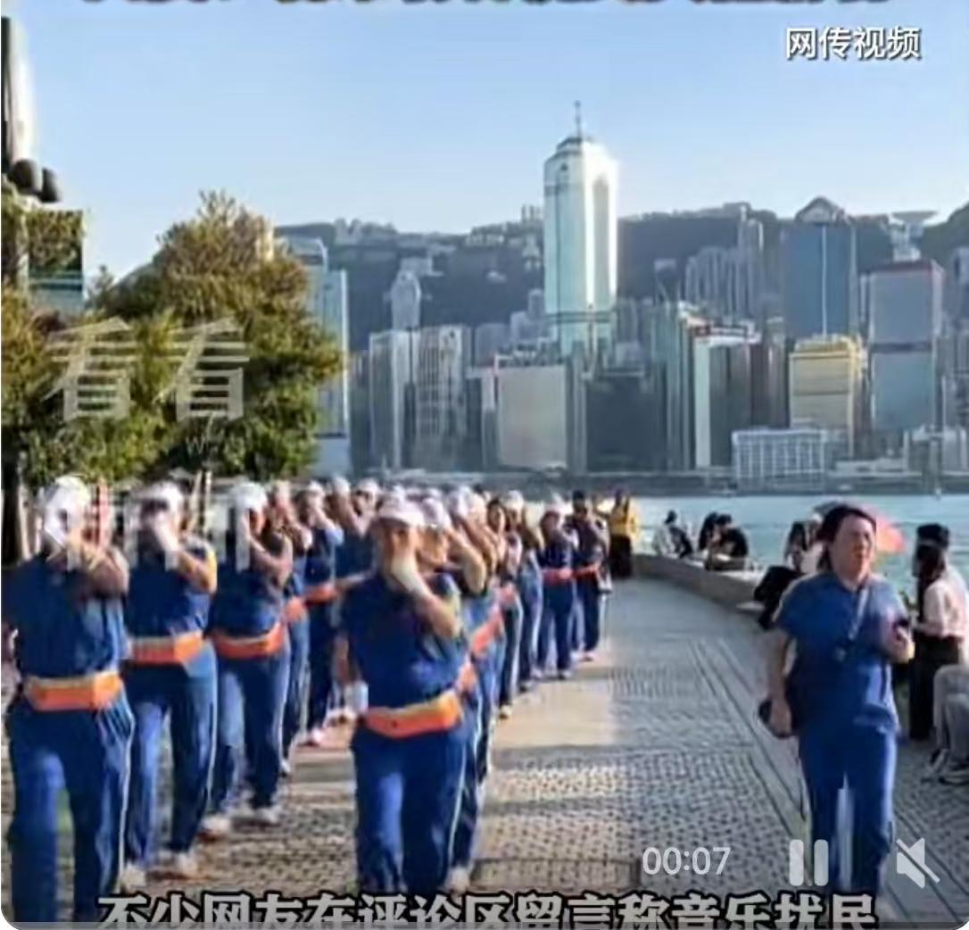 香港维多利亚港的晨光里，一群身着蓝色队服的老年人正沿着海岸线快步前行，随身音响播