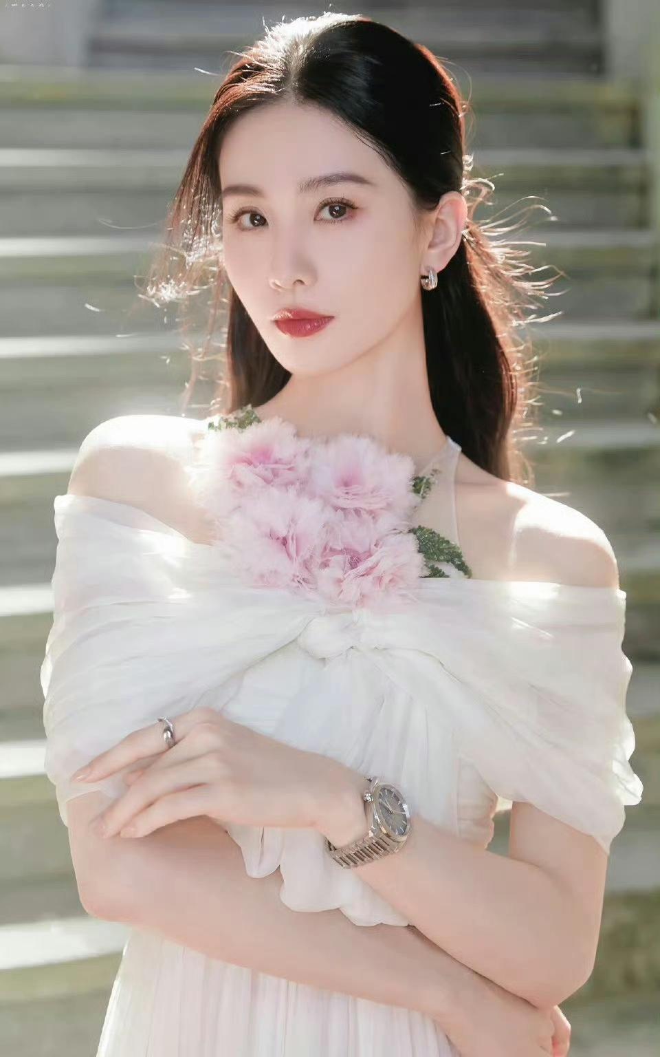 刘诗诗一袭白色露肩长裙，粉色花饰点缀其间，于光影与绿意中尽显温婉灵动。简约配饰衬