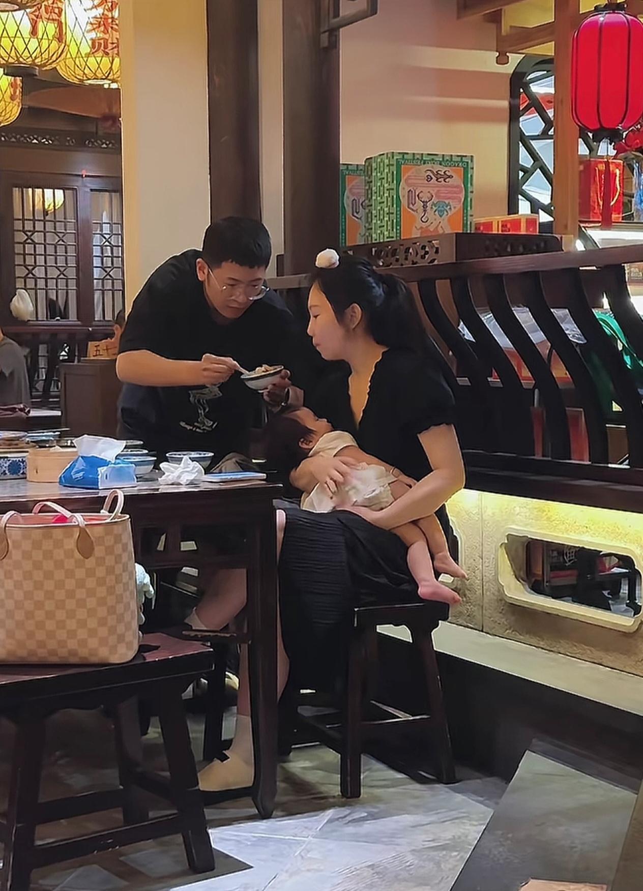 餐厅里最暖的一幕：妈妈抱着熟睡的宝宝，爸爸一口一口喂她吃饭，连碗都端得稳稳的。