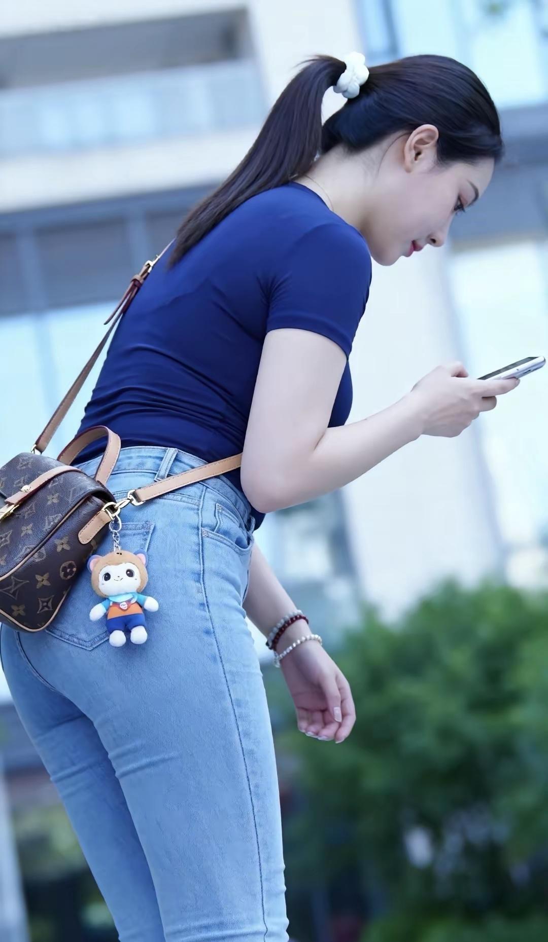 女生在户外看手机，背着可爱包包。