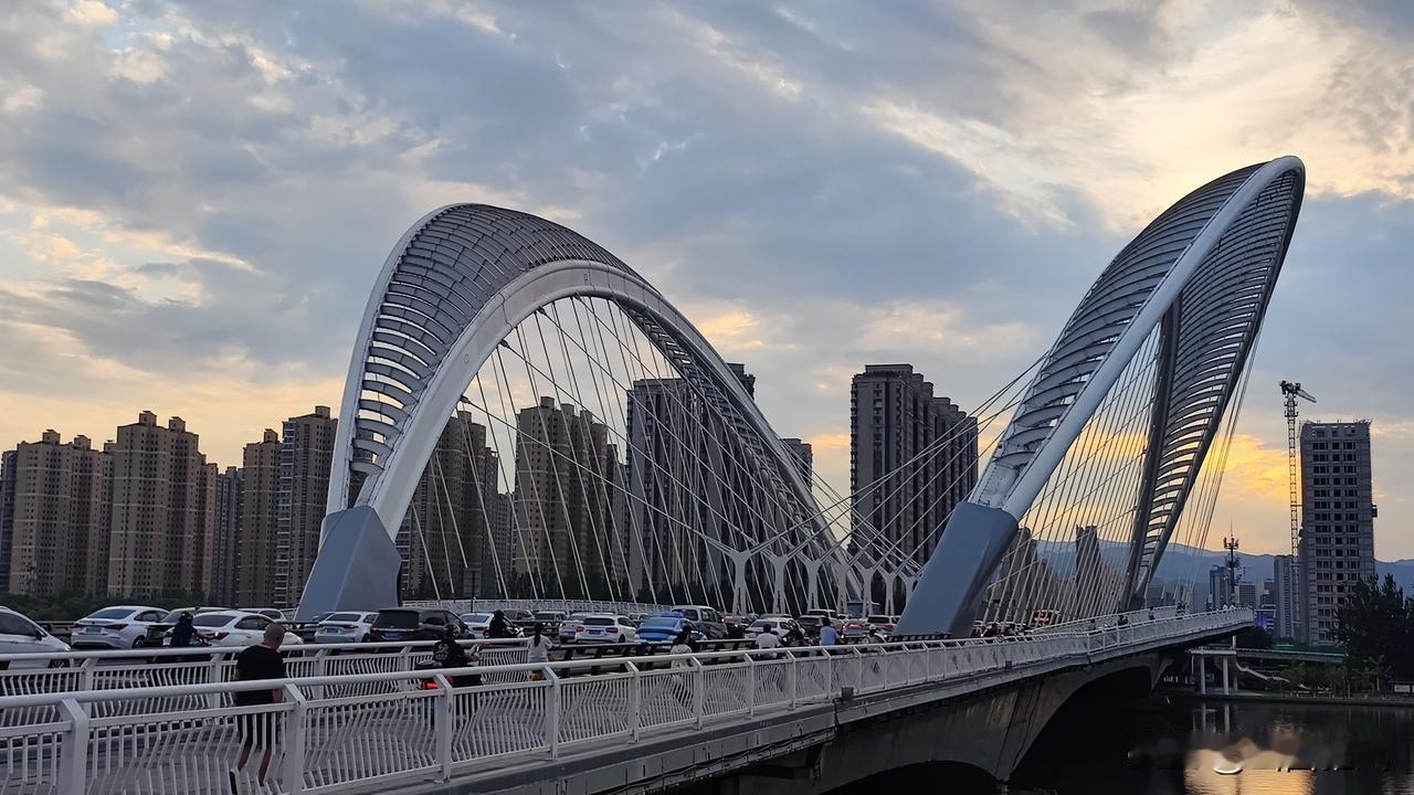 暮色漫过太原南中环桥，灰蓝云絮被夕阳吻成淡桔长带。车流与霞光交织，在汾河水面投下
