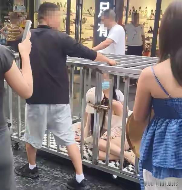 湖南汨罗市两名女子和一条黑狗被关进金属笼子，挂着写有“偷人的”纸牌，一群人推着笼