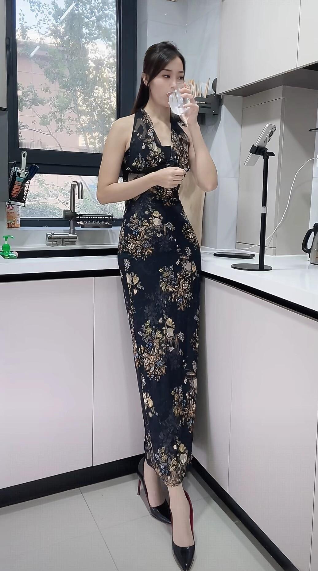 穿花裙子的女士在厨房喝水。